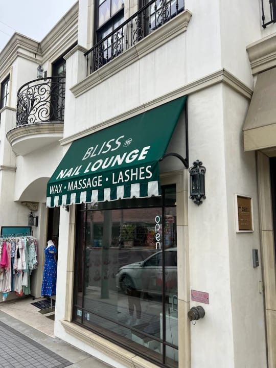 Bliss Nail Lounge on Highland Avenue in Manhattan Beach, with its green awning reading Wax, Massage, Lashes beneath iron balconies