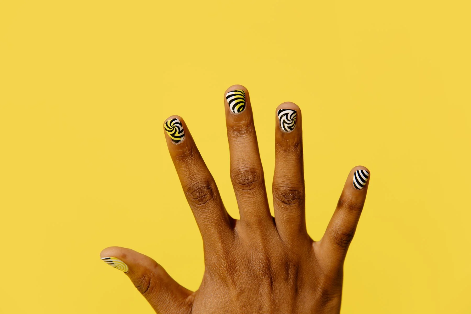 A hand with graphic patterned nail art against a yellow background.