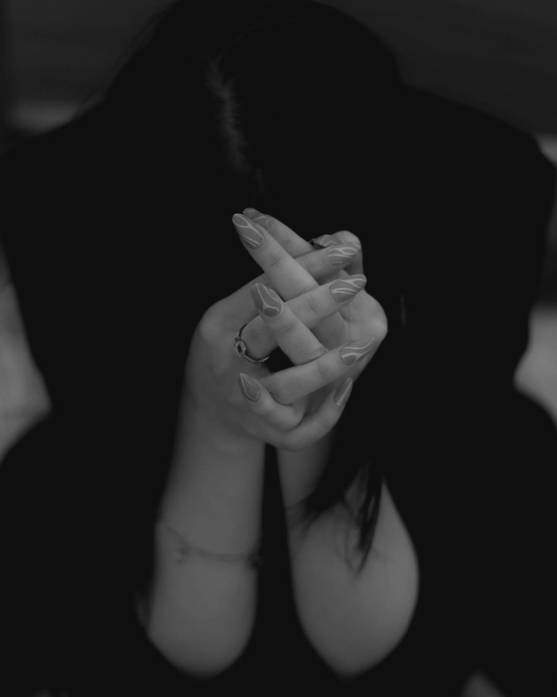 A black-and-white portrait with clasped manicured hands and dark clothing.