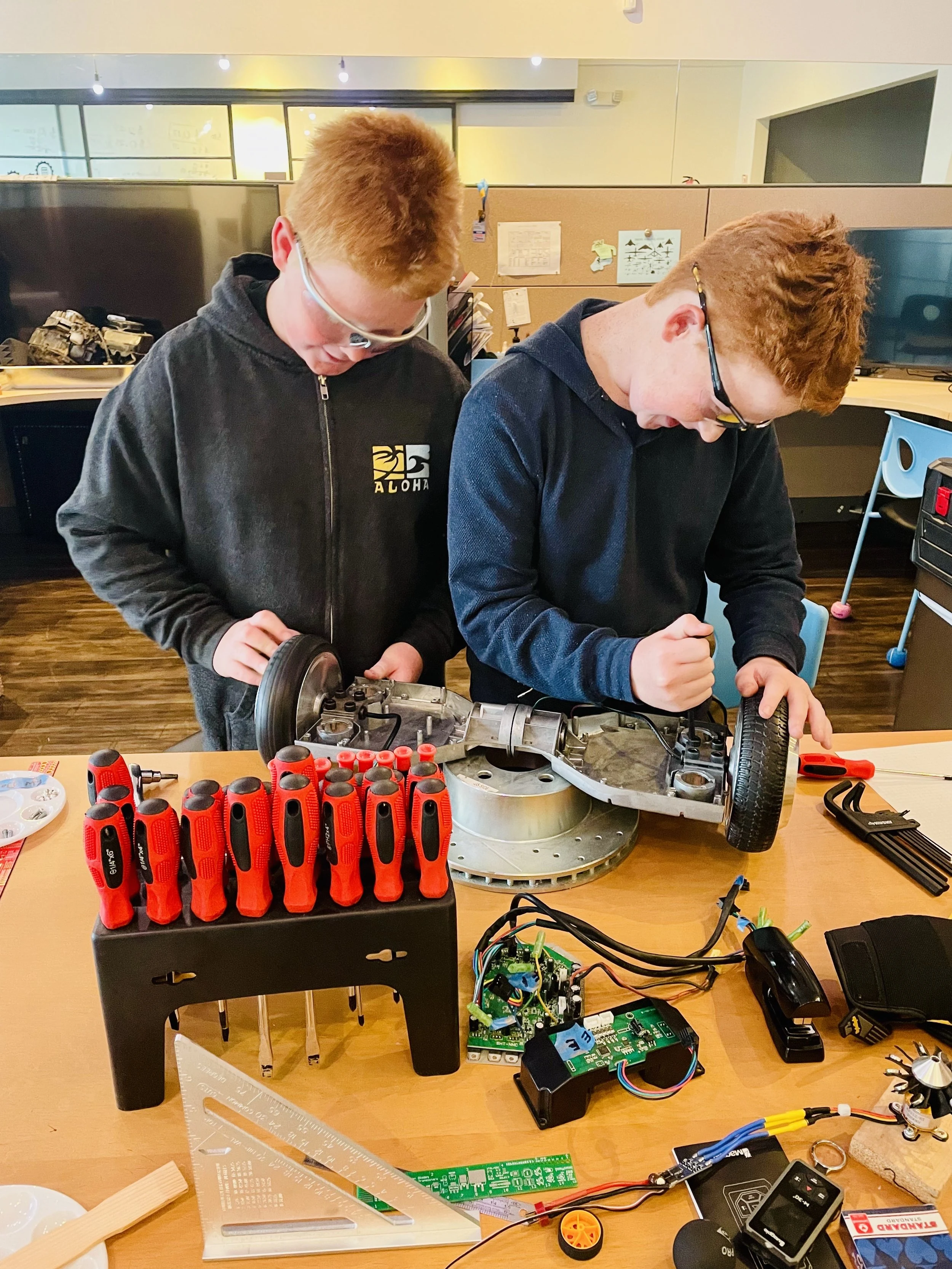 Students working with a hand tool at a project table.